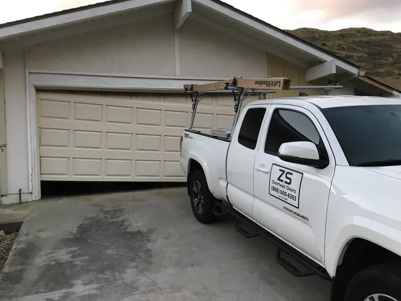 Beige garage door hanging crooked, lower on the right side, with the ZS Overhead Doors truck parked in front